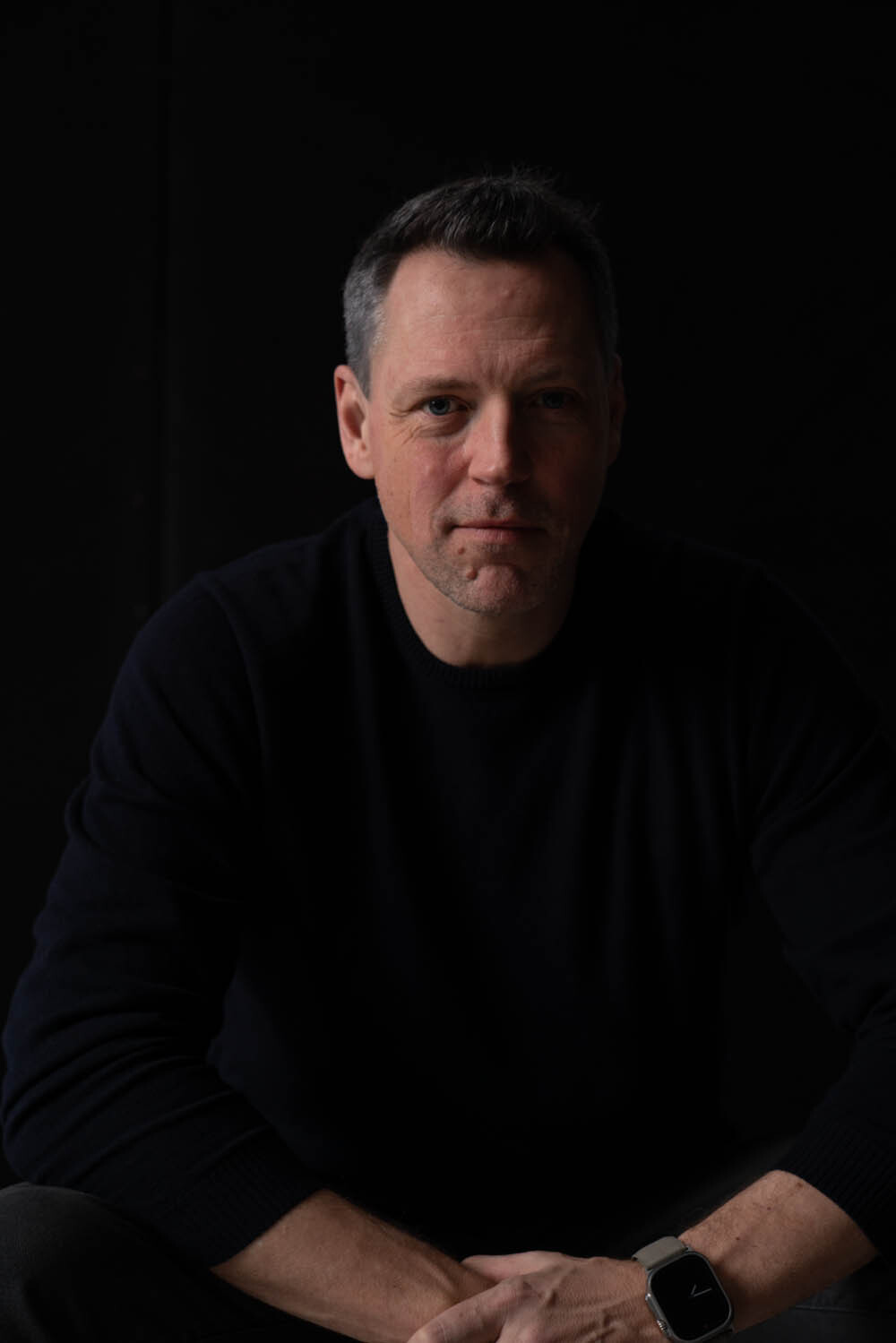 Oliver seated in a black sweater, looking directly at the camera