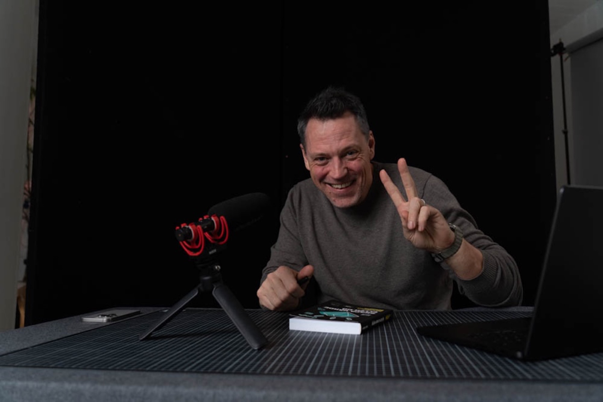 Oliver smiling beside a podcast microphone and making a peace sign